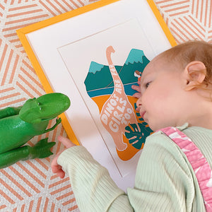 Girl laid with dinosaur toy and 'Dino's are for girls too' print