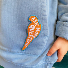 Load image into Gallery viewer, Embroidered kids red, white and blue iron on parrot shaped badge/patch featuring the words &#39;ask more questions&#39;. Sewn onto boys blue sweatshirt.
