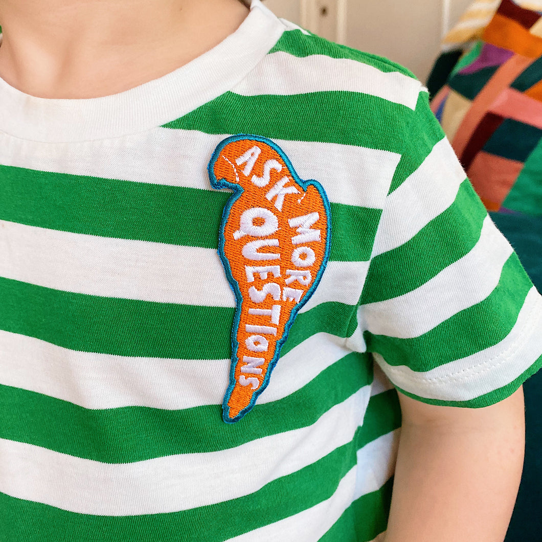 Embroidered kids red, white and blue sew on parrot shaped badge/patch featuring the words 'ask more questions'. Sewn onto children's T-shirt.